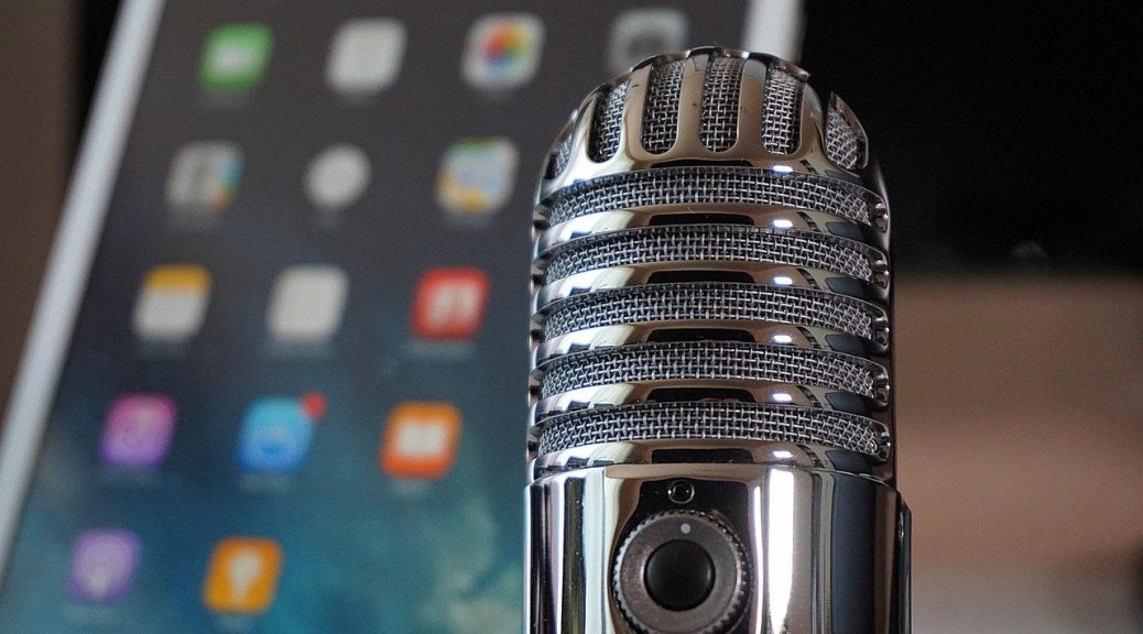 Image of a microphone with a smart phone or tablet in the background.